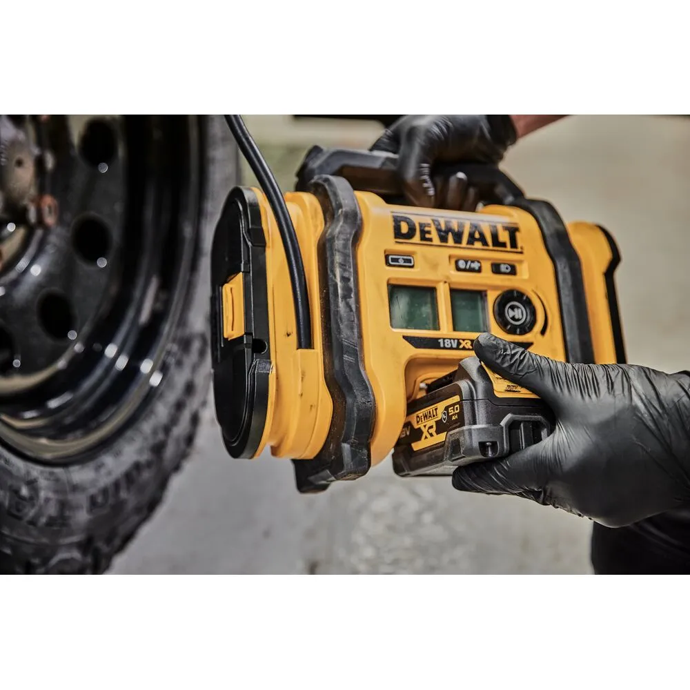 Pildil on näha DeWalt akutoitel kompressor, mida hoiab inimene, kes on pannud selga mustad kindad, pildil on näha ka...