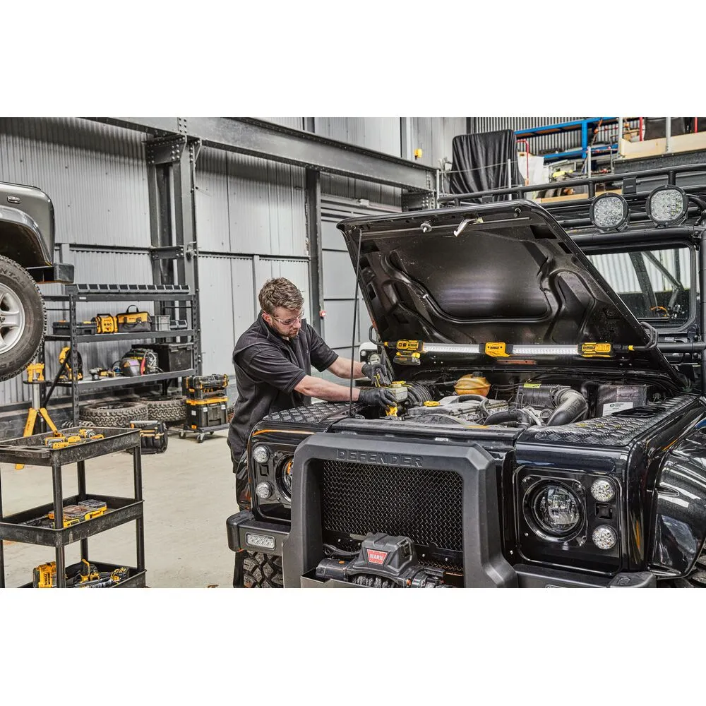 Pildil on mehaanik, kes töötab Dewalt kapotialuse LED-valgusti DCL045 abil Land Rover Defenderi mootori kallal.