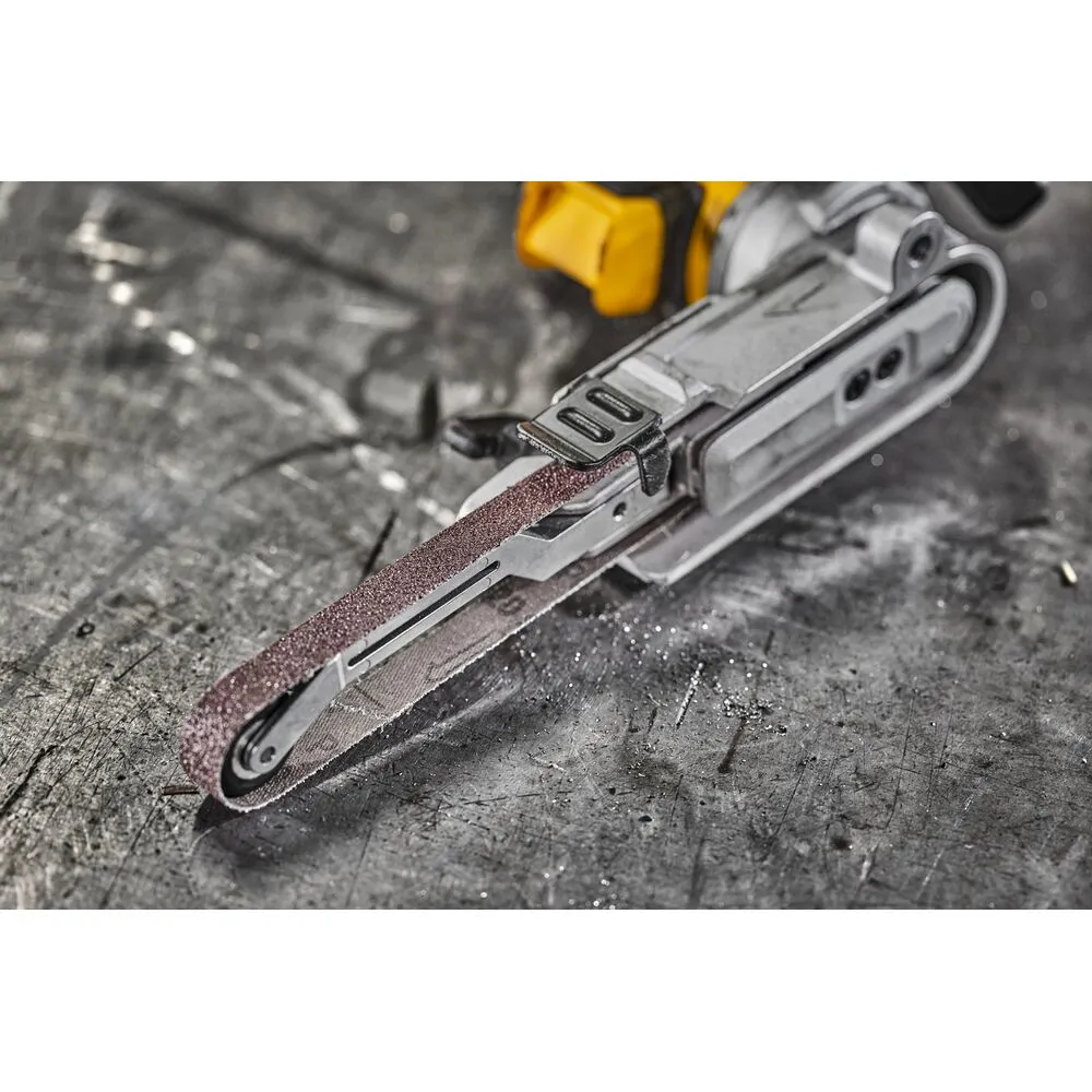 Pildil on DeWalt akulintlihvija DCM200E2T, mis on paigutatud tööpinnale ja mille rihma küljes on näha tolmu, mis viitab...
