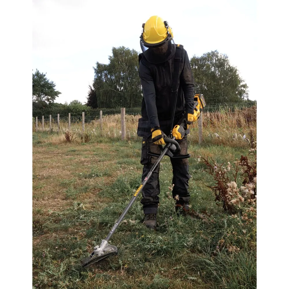 Pildil on näha mees kandmas kaitseriietust ja kiivrit, kes töötab põllul DeWalt 54V võsalõikuri otsikuga.