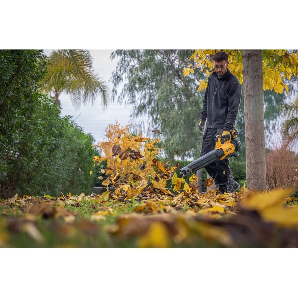 Pildil on näha mees, kes kasutab DeWalt akutoitega lehepuhurit DCMBL562P1, et puhuda lehti aiast.