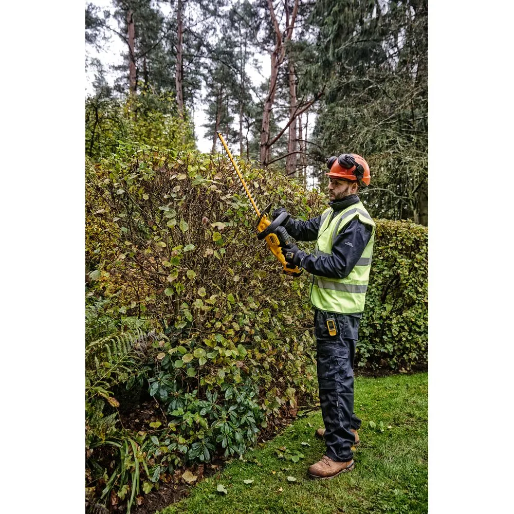 Pildil on mees, kes kasutab DeWalt akuhekipügajat DCMHT563N, ilma akuta ja laadijata, et pügada hekki väljas.