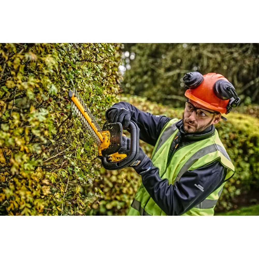 Pildil näeb meest, kes töötab DeWalt akuhekipügajaga DCMHT563P1, pügades rohelist hekki, kandes samal ajal kaitsevarustust.
