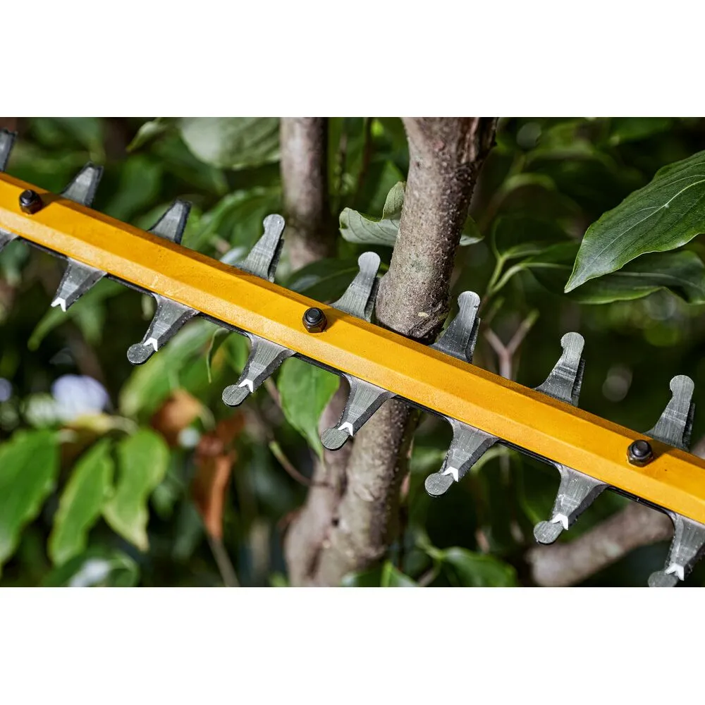 Pildil on näha DeWalt akutoitega hekipügaja DCMHT573N detail, mille terad on suunatud vastu puud ja rohelisi lehti.