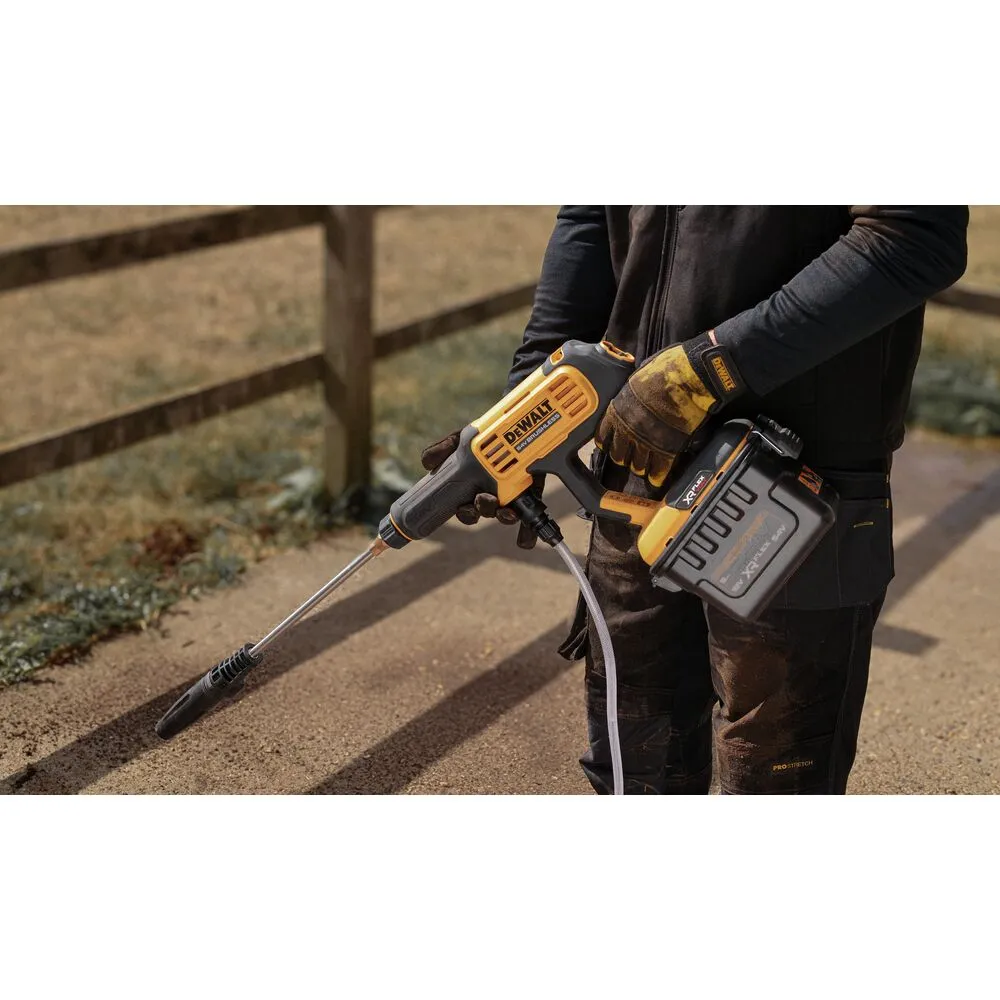 Pildil on inimene, kes hoiab käes DeWalt akusurvepesurit DCMPW1000N, mis on suunatud maapinnale.