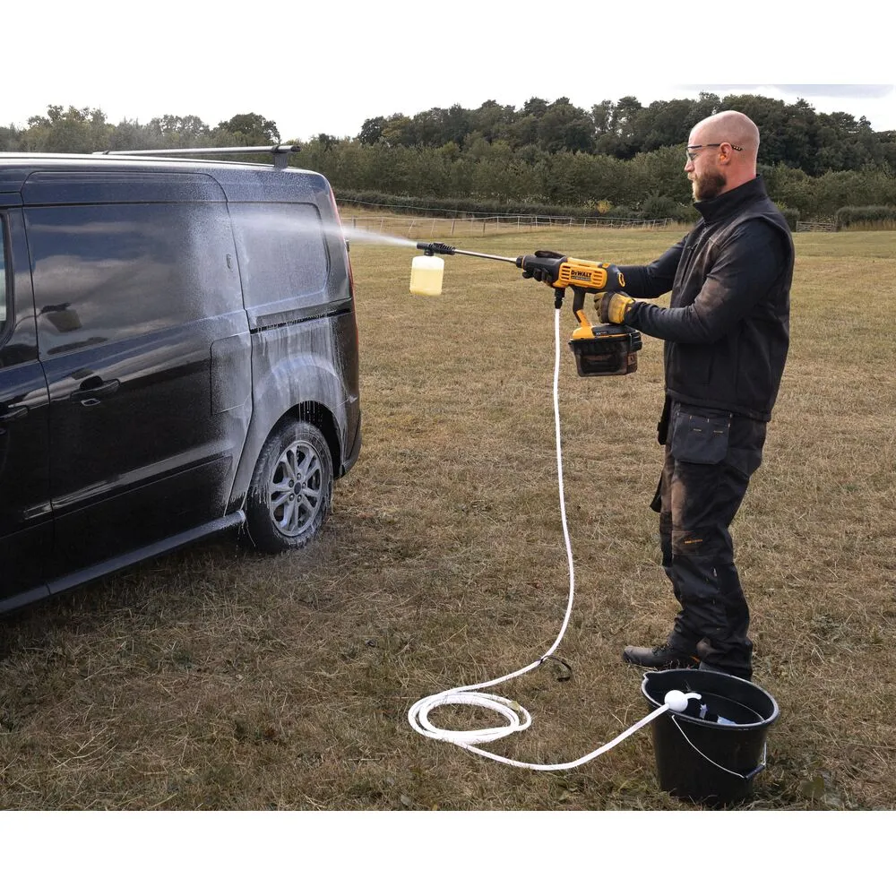 Pildil on mees, kes kasutab DeWalt akusurvepesurit DCMPW1000N, et pesta musta autot põllul.