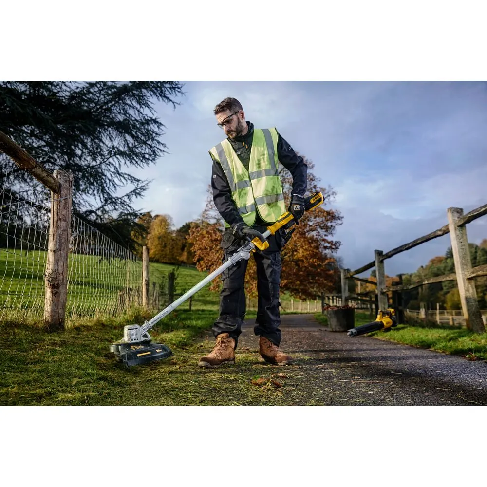 Pildil on Dewalt akutrimmer DCMST561P1, mida hoiab mees, kes seisab rohelisel alal.