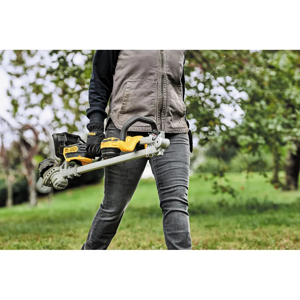 Pildil on näha DeWalt akutrimmer DCMST561P1, mis lõikab muru ja viskab seda kõrvale.