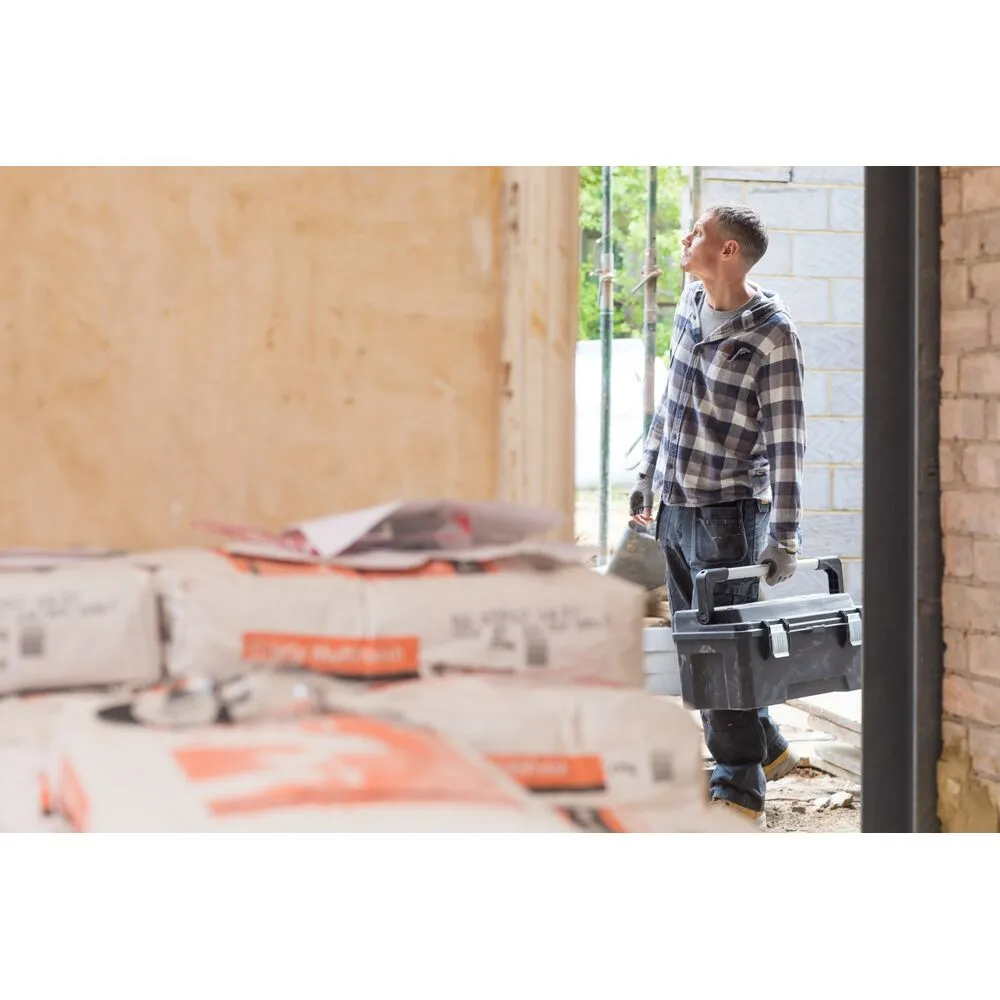 Pildil on mees, kes kannab oma käes Stanley tööriistakasti FATMAX FMST1-75791 ehitusplatsil.