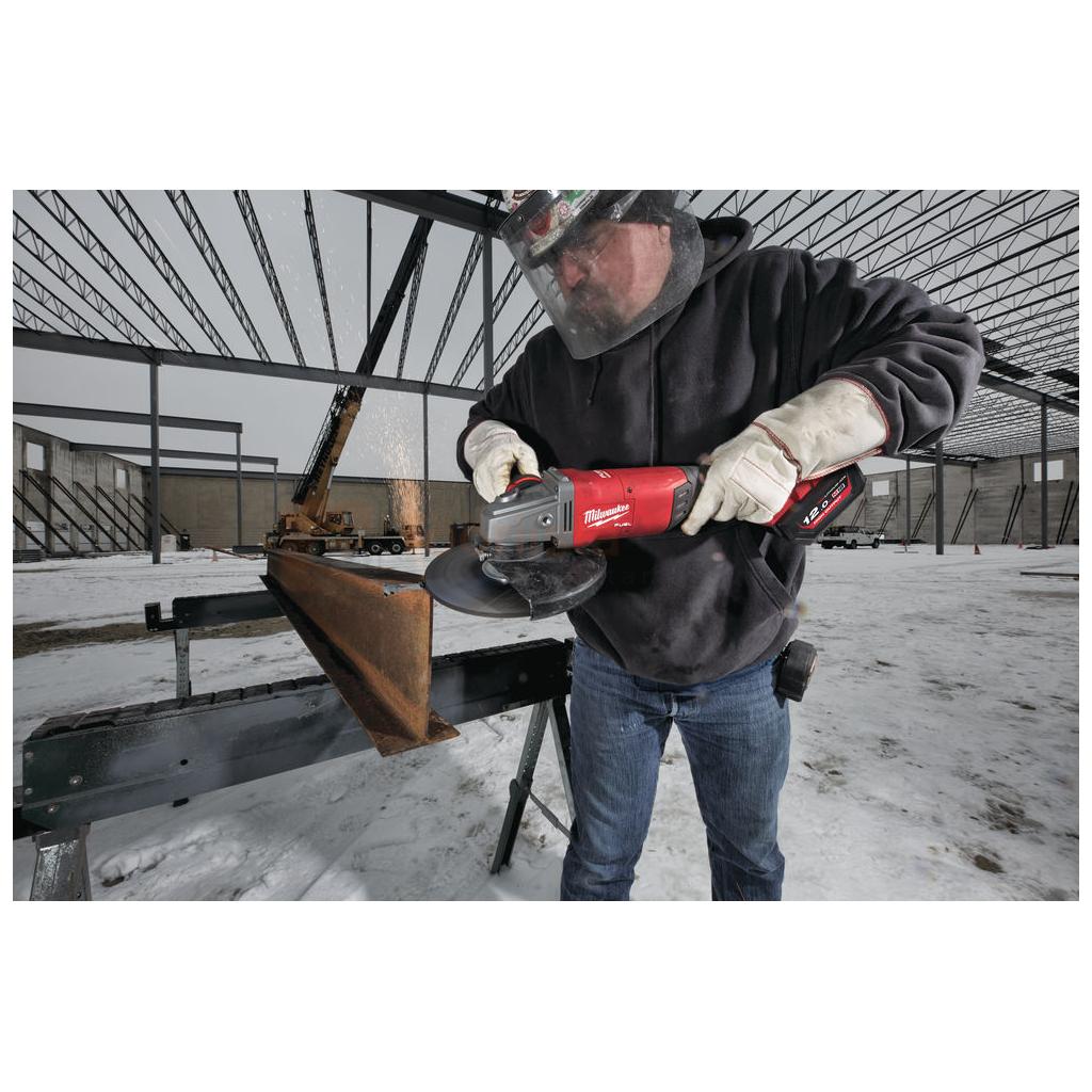 Pildil on mees, kes kasutab Milwaukee akunurklihvija M18 FLAG230XPDB-0C, et lihvida metalli väljas lumises keskkonnas.