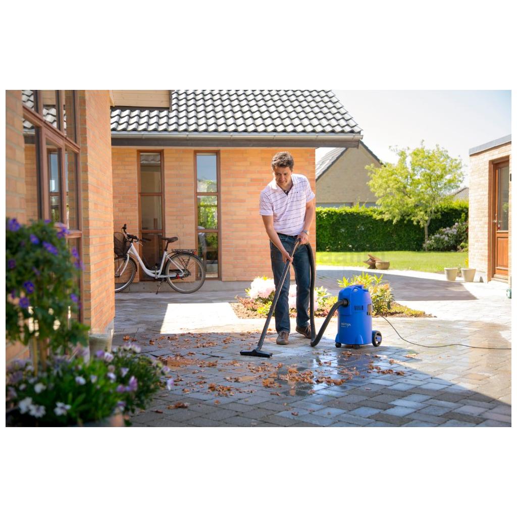 Pildil on mees, kes kasutab Nilfisk Buddy II 18 vee- ja tolmuimejat, et puhastada õuest sillutist lehtedest ja mustusest.